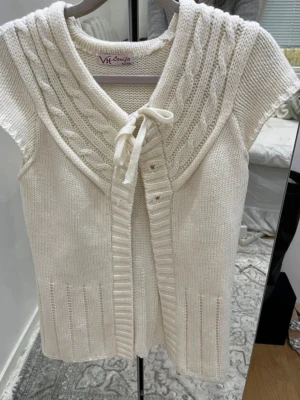 Vit stickad kofta med knyt från V.H. Louifa - Säljer en krämvit stickad kofta från V.H. Louifa med korta ärmar och snygg kabelstickad detalj vid axlarna. Står XL men den sitter som en S/M. 