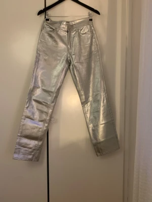 Silvriga raka byxor i metallic - Säljer ett par riktigt snygga byxor i metallic silver med rak passform. Byxorna har klassisk femficksdesign och stängs med knapp och dragkedja. 