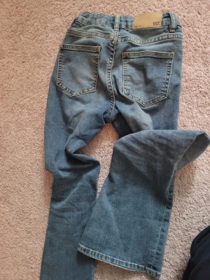 Blå flare jeans från 157, storlek 150 - Säljer ett par blå jeans från 157 i modellen Skippy Flare. Byxorna har utsvängda ben, fickor fram och bak och justerbar midja med resår.