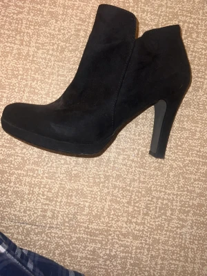 Svarta stövletter med klack - Säljer ett par svarta stövletter från Keen med rund tå och hög klack. Skorna är gjorda i mocka och har dragkedja på sidan för enkel på- och avtagning. Perfekta för dig som gillar stilrena och snygga boots med lite höjd. Svart färg passar med allt och dom är riktigt snygga till jeans. 