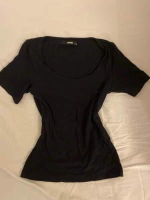 Svart topp från BikBok med rund hals - En enkel svart topp från BikBok i storlek XS. Modellen har korta ärmar och en rundad, djup halsringning. Materialet känns mjukt och stretchigt, perfekt för att styla med jeans eller kjol. Snygg och stilren design som funkar till många looks.jätte skön och lite tjockare material som gör att den sitter extra fint i midjan