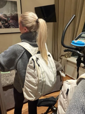 Vit ryggsäck Douchebag - Säljer en stilren vit ryggsäck Douchebag med flera dragkedjefack och vadderad baksida med logotyp. Ryggsäcken har breda axelband och är tillverkad i ett tåligt syntetmaterial. Perfekt för dig som vill ha en clean och modern look.