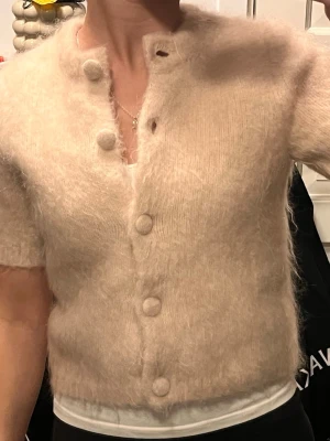 Beige fluffig kofta med stora knappar - Supersöt ljus rosa kofta med korta ärmar och stora tygklädda knappar framtill. Koftan är fluffig och har en croppad passform som ger en trendig look. Perfekt att slänga över ett linne för en mysig vibe. Jag har bara använt den 2 gånger så den är som ny!😍 		 Består av: Mohair 38%, Ull 38%, Polyamid 19%, Elastan 5% 