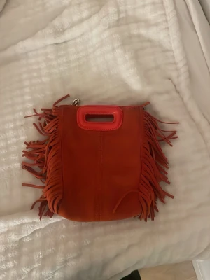 Orange axelväska med fransar från Maje - Intressekoll på min jättecoola maje väska. Den är en jättenöjd orange färg och har tecken av användning. Går att använda både som axelväska men också att bara hålla i handen 🥹🥹🥹💖💖💖