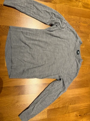 Grå långärmad tröja i merinoull från Uniqlo - En stilren grå långärmad tröja från Uniqlo i mjuk merinoull. Tröjan har rund halsringning och en normal passform. Enkel och clean look som funkar till det mesta