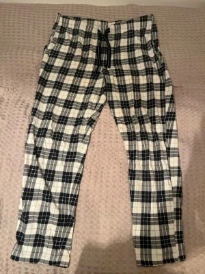 Svarta och vitrutiga pyjamasbyxor från Kappahl - Rutiga byxor från Kappahl i storlek M. De har svart och vit färg, elastisk midja med snörning och ett loose fit. Materialet är mjukt och känns som bomull, perfekt för chill dagar. Klassisk rutig design som sticker ut.
