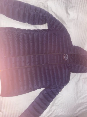 Blå pufferjacka från Save The Duck - Säljer en blå pufferjacka från Save The Duck i storlek S. Jackan är skön  med horisontella quiltade partier och har en orange logga på ärmen. Dragkedja framtill med orange detaljer. Perfekt för dig som vill ha en snygg och funktionell jacka.