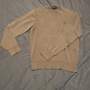 Beige v-ringad tröja från Pierre Cardin - Klassisk beige v-ringad tröja från Pierre Cardin med diskret broderad logga på bröstet. Tröjan har långa ärmar, ribbade muddar och är tillverkad i ett mjukt material som passar perfekt till vardags.