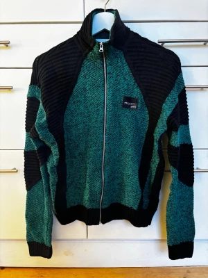 Grön och svart stickad kofta från Adidas. Oanvänd! - Säljer en unik stickad kofta i bomull från Adidas Equipment med grönmelerad bas och svarta ribbade partier på axlar, ärmar och sidor. Tröjan har hel dragkedja framtill, hög krage och Adidas Equipment-märke på bröstet. Osnvänd! Storlek UK 8/ 34-36