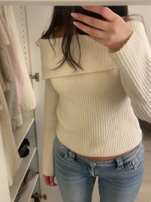 Offshoulder stickad tröja - Säljer en ljus, offshoulder stickad tröja med ribbad struktur. Tröjan har lång ärm och sitter snyggt med en perfekt passform. Perfekt för dig som gillar stilrena och trendiga plagg med lite extra edge.
