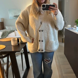 Beige stickad kofta med knappar - Mysig beige stickad kofta med grov ribbad struktur och stora svarta knappar framtill. Koftan har två praktiska fickor och en oversized passform. Perfekt att slänga över en t-shirt för extra lager!!💕