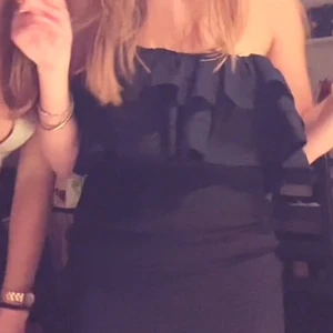 Svart axelbandslös topp - Säljer en svart axelbandslös topp med snygga volangdetaljer upptill. Toppen är kort och har en slim passform som framhäver figuren. Perfekt för dig som gillar en stilren look med lite extra edge.