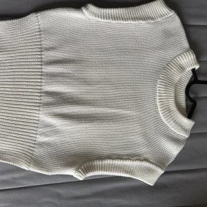 Vit stickad väst  - Snygg vit stickad väst med ribbade kanter vid hals, ärmöppningar och midja. Den är perfekt att styla över en skjorta eller t-shirt 