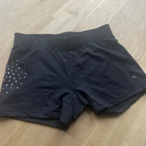 Svarta träningsshorts med diamanter - Svarta shorts från Casall i stretchigt material, perfekta för träning. De har en bred resår i midjan och är dekorerade med silvriga diamanter på ena sidan. Snygg och sportig look med kort passform som sitter tajt.
