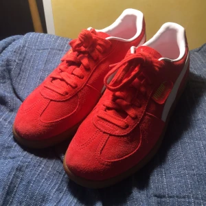 Puma Palermo röda sneakers mocka - Säljer ett par Puma Palermo sneakers i röd mocka med vita detaljer och gummisula (slutsåld nästan överallt). Skorna har snörning, rund tå och klassisk Puma-logga i guld på hälen och sidan. Säljer då skorna var en aning för stora och jag inte hann returnera. Köpte skorna för 1050kr. Helt oanvända.