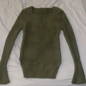 Olivgrön ribbad stickad tröja - Säljer en olivgrön stickad tröja med ribbad struktur och långärmad design. Tröjan har en rundad halsringning och är figurnära med lite längre ärmar. Perfekt för dig som gillar enkel men snygg stil och vill ha något mjukt och bekvämt.
