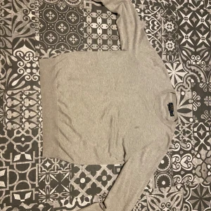 Grå tröja från Polo Ralph Lauren - Snygg grå tröja från Polo Ralph Lauren i mjuk pima bomull. Klassisk rund hals och diskret broderad logga på bröstet. Perfekt passform med långa ärmar och ribbade muddar. Enkel och stilren design som funkar till allt.