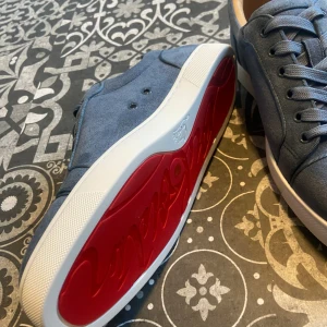 Blå Christian Louboutin sneakers - Snygga blå sneakers från Christian Louboutin med klassisk röd sula och vit kant. Skorna har rund tå, snörning och är tillverkade i mocka med ventilerande hål på sidan. Insidan är mjukt fodrad i beige skinn för extra komfort. Perfekt för dig som gillar exklusiva detaljer. PRIS KAN DISKUTERAS ( bekräftelse kort på sista bilden)