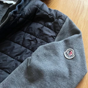 Moncler cardigan med huva - Säljer en grå Moncler cardigan med insydd hoodie🙌🏻| Storlek L | Skick 9/10🔥| Skriv vid minsta fundering 💭 