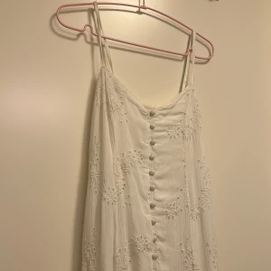 Supersöt vit långklänning - Superfin vit långklänning med tunna axelband och broderade blommor över hela klänningen. Klänningen har en rad vita knappar från topp till tå, det är en split också längst ner på klänningen i mitten. Helt okej skick eftersom att jag själv köpte den second hand❤️