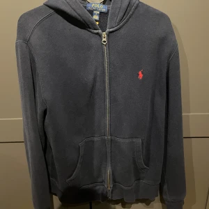 Mörkblå zip från Polo Ralph Lauren - Riktigt snygg polo zip. Storlek 14-16 år. Den är använd men fint bevarad. Inga skador. Väldigt populär och snygg.