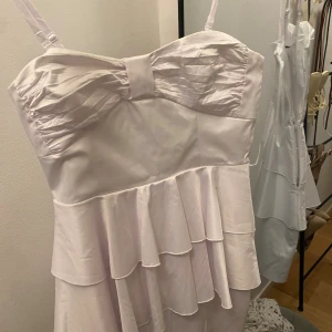 Ljusrosa volangklänning från Zoul - Supersöt ljusrosa klänning från Zoul med tunna axelband och snyggt rynkad överdel. Klänningen har flera lager volanger nedtill som ger en extra flirty vibe. Materialet är glansigt och känns lyxigt, perfekt för dig som vill sticka ut lite extra.