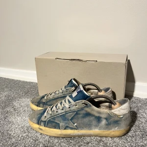 Blå GGDB sneakers med stjärndetalj - Säljer ett par GGDB sneakers i blått med slitna detaljer och ikonisk stjärna på sidan. Skorna har beige snörning, gult vintagesliten sula och GGDB-logga på plösen. Ovandelen är i canvas med en cool, tvättad look och svarta yttersulor. Perfekta för dig som gillar streetstyle. Köpte från sicurofashion för 3599kr