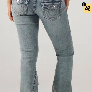 True Religion bootcut jeans ljusblå - Snygga ljusblå jeans från True Religion med klassiska U-formade sömmar på bakfickorna och silverfärgade knappar. Modellen har bootcut-ben och låg midja, tillverkade i mjukt jeanstyg med slitna detaljer för en cool vibe.