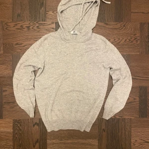 Ljusgrå hoodie från BVALDI - Mysig ljusgrå hoodie från BVALDI med huva och snörning. Tröjan är stickad i mjuk kash/merino blandning och har ribbade muddar vid ärmslut och nederkant. Liten broderad logga på bröstet ger en clean look. Perfekt för chill dagar. Nypris ca 1299 (litet hål på vänster armbåge) fråga om vad som helst