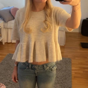 Beige stickad croppad topp med volang - Superfin beige stickad topp med korta ärmar och volang nedtill. Sitter skitsnyggt och passar perfekt med ett par jeans till. Säljer då den endast kommit till användning en gång. Den är som ny💗💗💗