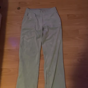 Ljusgröna mjukisbyxor Juicy Couture - Ljusgröna mjukisbyxor från Juicy Couture med broderad JC-logga på fickan. Byxorna har bred resår i midjan med hål för snörning, stora fickor fram och en bakficka med tryckknappar. Mjukt material som känns skönt mot huden.