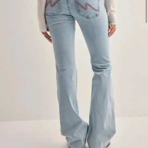 Bootcut ljusblå jeans med slitningar - Säljer ett par ljusblå bootcut jeans med slitna knän och broderade detaljer på bakfickorna. Jeansen har klassisk femficksdesign och är tillverkade i denim. ( dom är lite slitna längs ner då dom är vite långa på mig 166) 