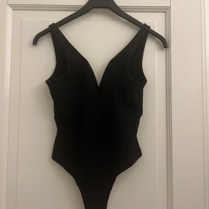 Svart body med v-ringning - Snygg svart body med djup v-ringning och breda axelband. Enkel och stilren design som ger en modern look. Perfekt för fest. Materialet känns mjukt och stretchigt för en bekväm passform. Säljer då den tyvärr är för liten🥺🥰