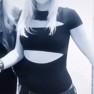 Svart croppad topp med cutouts - Säljer en svart, croppad topp med coola cutouts över bröstet och magen. Toppen har korta ärmar och en tight passform som framhäver figuren. Perfekt för dig som vill sticka ut med en edgy och trendig look.