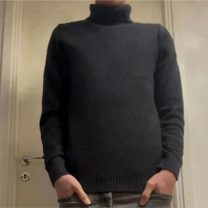 Svart nacktröja från Jack & Jones - Snygg svart polotröja från Jack & Jones med ribbade muddar och hög krage. Tröjan är stickad och har en klassisk, enkel design som funkar till jeans eller chinos. Perfekt för dig som gillar stilrena och bekväma plagg med lite edge.