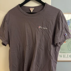 Lila Champion t-shirt i bomull - Säljer en lila t-shirt från Champion i storlek Large. T-shirten har korta ärmar, rund hals och klassisk Champion-logga broderad på bröstet samt på ärmen. Materialet är mjuk bomull och passformen är normal. Perfekt för en chill och sportig look.