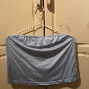 Ljusblå bandeau tubtopp - Säljer en enkel och stilren ljusblå bandeau tubtopp. Toppen är axelbandslös och har en mjuk, slät yta i ett stretchigt material som sitter bekvämt mot kroppen. Perfekt för dig som gillar minimalistisk stil och vill ha en topp som är lätt att matcha.