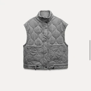 Grå quiltad väst med snörning från Zara - Säljer en grå quiltad väst med hög krage och två stora fickor framtill. Västen har snörning nedtill och ett unikt mönster i sömmarna. 