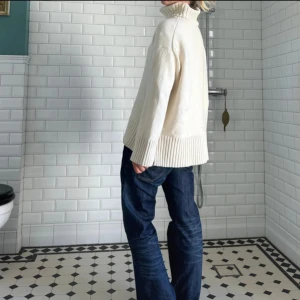 Vit polotröja med bred ribbad kant - Säljer en vit polotröja med bred ribbad kant nertill och vid ärmsluten. Tröjan har hög, rejäl polokrage och är stickad i ett mjukt material. Passformen är loose och ärmarna är långa, perfekt för kyliga dagar.