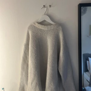 Oversized ljusgrå stickad tröja - Mysig oversized stickad tröja i ljusgrått med bred ribbad kant vid hals, ärmslut och nederkant. Tröjan har en avslappnad passform och långa ärmar, perfekt för att hålla sig varm under kyliga dagar. Enkel och stilren design som är lätt att matcha.