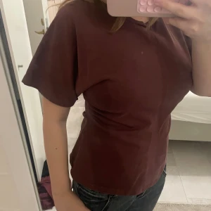 Mörkbrun t-shirt med kort ärm - En enkel och stilren mörkbrun topp med korta ärmar och rund halsringning. Modellen är rak och passar perfekt till jeans eller kjol. Materialet känns mjukt och bekvämt mot huden.