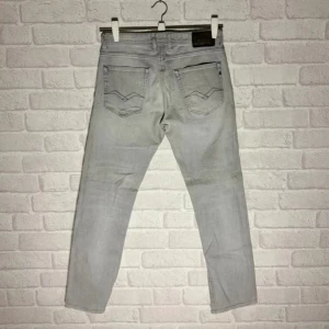 Replay ljusgrå jeansbyxor herr - Snygga ljusgrå jeansbyxor från Replay med klassisk femficksdesign och svarta detaljer vid fickorna. Byxorna har raka ben och normal passform, perfekta för en avslappnad stil. Tillverkade i mjukt jeanstyg för skön känsla hela dagen.