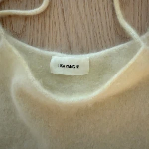 Ljusbeige linnetopp från Lisa Yang - Supermjuk och fluffig ljusbeige linnetopp från Lisa Yang med tunna axelband. Toppen har en enkel, rak passform och är stickad i ett lyxigt material som känns riktigt skönt mot huden. Perfekt för dig som gillar minimalistisk och stilren design.