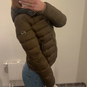 Olivgrön pufferjacka från colmar - Snygg olivgrön pufferjacka från colmar. Jackan har två fickor med dragkedja och en diskret logotyp på ärmen. Passformen är normal och jackan är perfekt för kyliga dagar. Den har några skavanker (två sista bilderna) men reporna synns knappt.