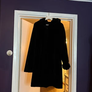 Svart pälsjacka med huva KappAhl - Svart pälsjacka från Number One by KappAhl i storlek 42/44. Jackan har en oversized look, huva och långa ärmar med mjuka muddar. Perfekt för kalla dagar och har en riktigt mysig vibe. Snygg och enkel att matcha med din stil.