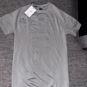 Gymshark onyx 3.0 - Snygg grå t-shirt från Gymshark med diskret logga på bröstet. Modellen har rund hals och korta ärmar, tillverkad i lätt och ventilerande polyester som passar perfekt för träning. Stilren design med en något slim passform och sportig känsla.