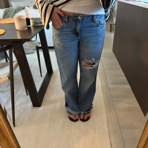 Snygga jeans  - Säljer ett par blåa straight fit jeans från GinaTricot i storlek 38. Jeansen har en snygg sliten detalj med hål på ena låret. De är i wide leg modell!💕