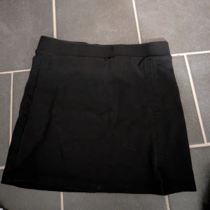 Svart kortkjol från Gina Tricot stl 246-152 - Svart, stilren kortkjol från Gina Tricot med enkel design och bred linning. Kjolen är gjord i mjukt bomullsmaterial och passar perfekt till en cool och avslappnad look. Snygg att matcha med crop tops eller hoodies för en trendig vibe.