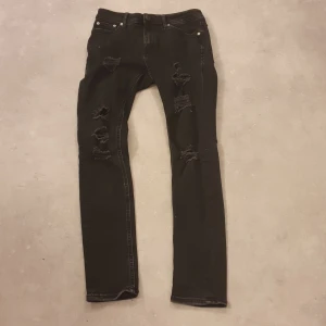 Svarta skinny jeans med slitningar - Svarta skinny jeans från Jack & Jones, modell Liam. Jeansen har flera slitningar och hål på benen för en cool, trendig look. Klassisk femficksmodell med smal passform. Perfekta för dig som gillar streetstyle.
