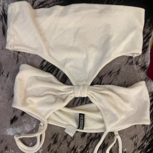Krämvit bikini från Chiquelle - Superfin krämvit bikini från Chiquelle med bandeau-topp som har knyt i mitten och matchande höga bikinitrosor. Materialet är mjukt och strukturerat, vilket ger en lyxig känsla. Perfekt för strandhäng och poolparty!